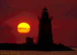 Lighthouse silhouette with sun ball in the background.